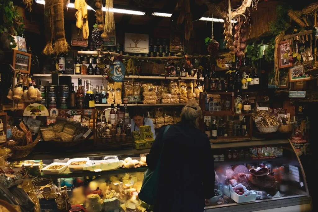 Local Italian deli counter stacked with pasta, cheeses, cured meats, and shopper