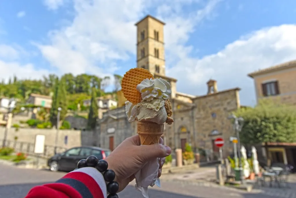 Hand holding gelato cone with Lucca church tower blurred in background
