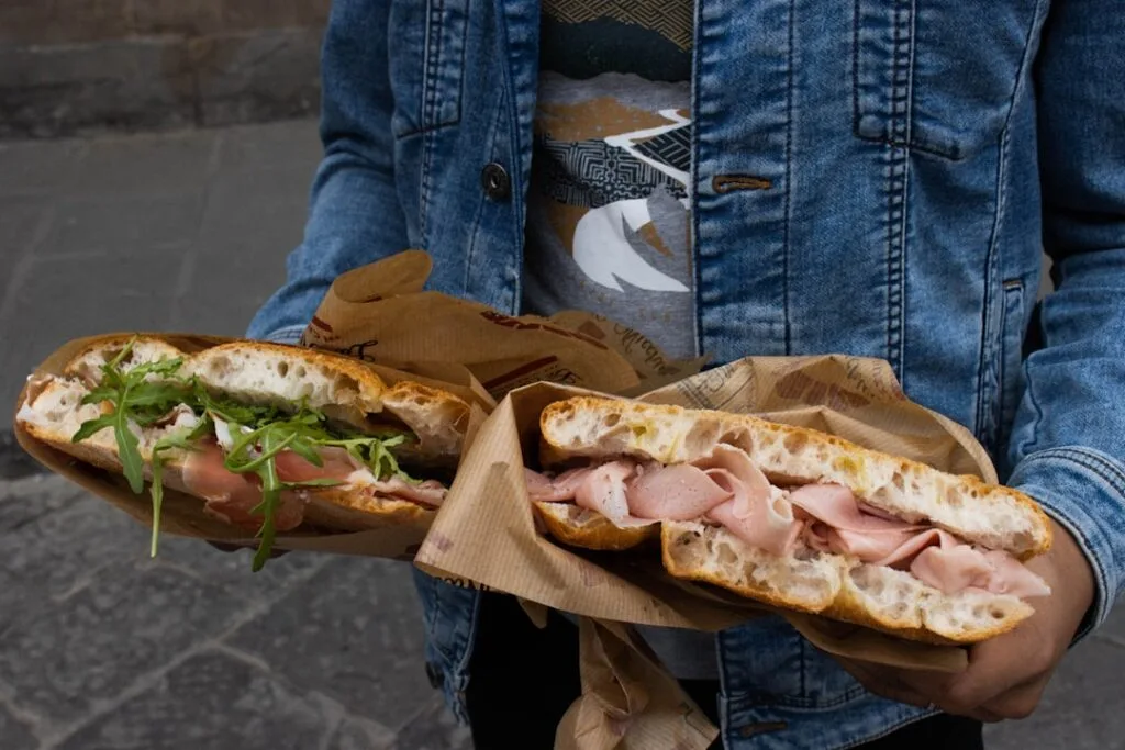 Person holding two prosciutto panini wrapped in paper on Lucca street