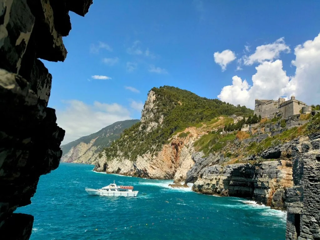 White boat navigating turquoise water along rugged Cinque Terre coastline