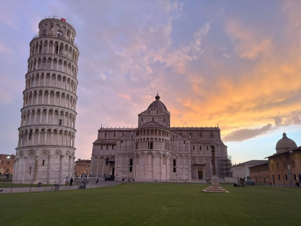 Pisa's Leaning Tower and cathedral under a colorful sunset sky