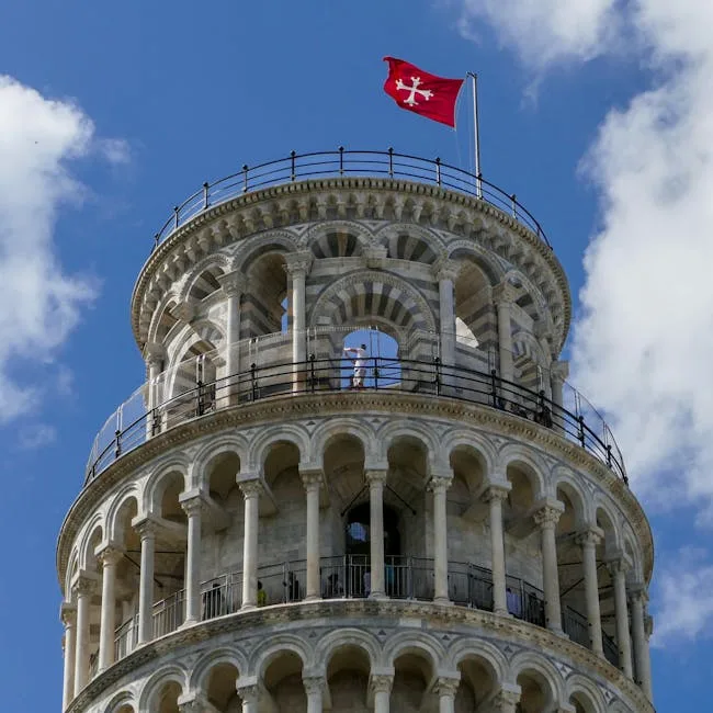 Leaning Tower of Pisa's upper tiers with red flag against sky