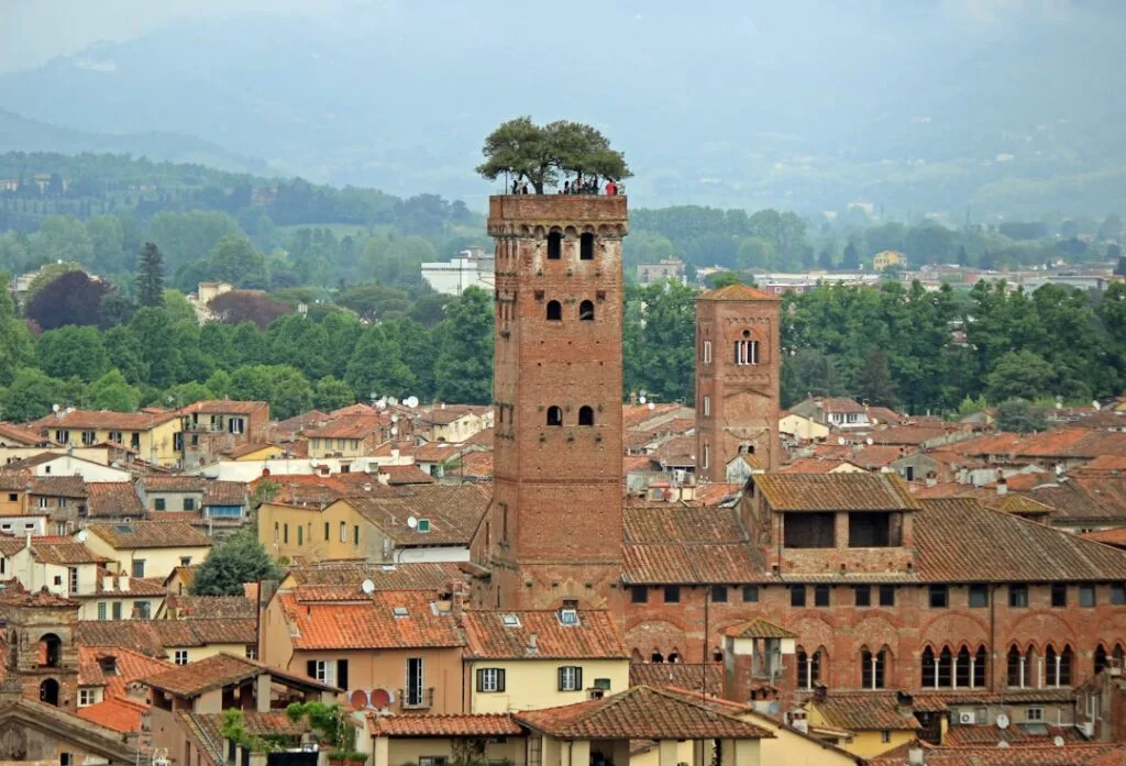 Brick medieval tower with rooftop trees rising above Lucca's terracotta rooftops