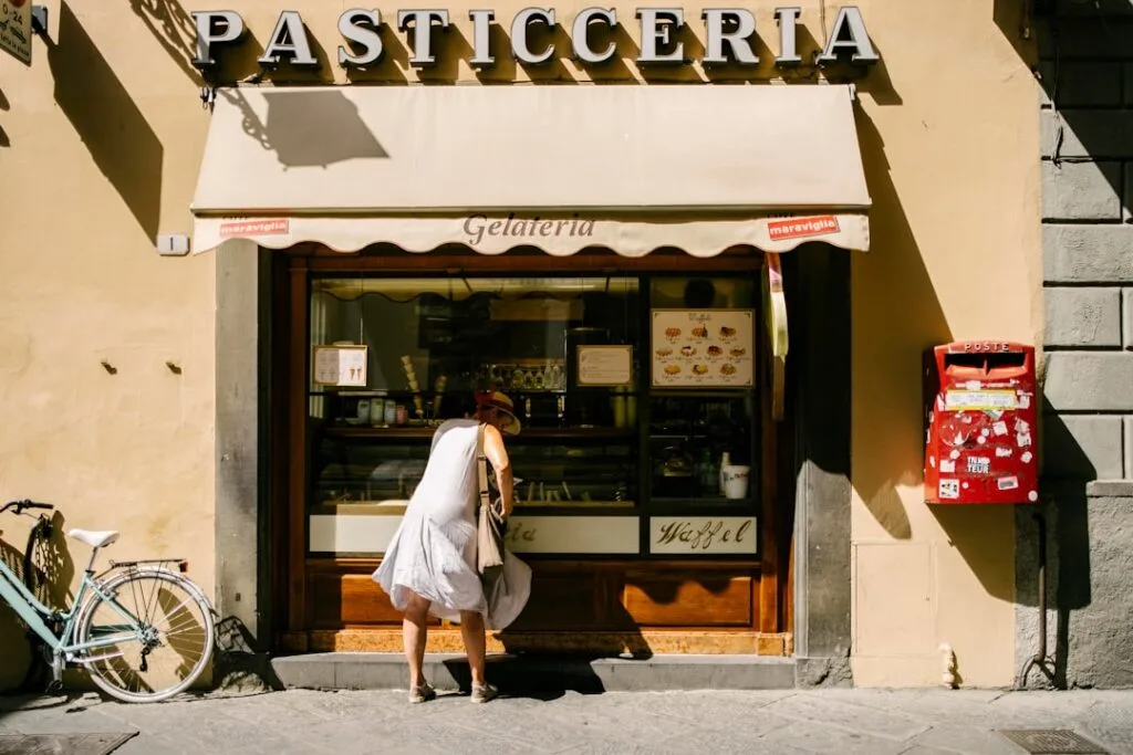 Customer leaning into a pasticceria window beneath awning in Lucca
