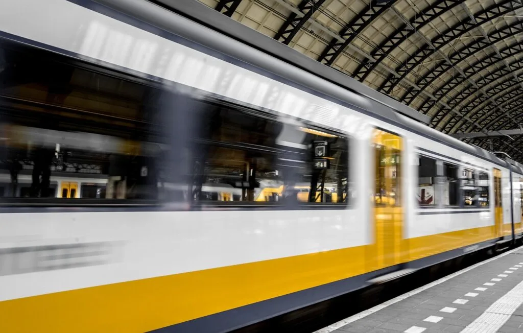 Yellow and white train speeding through a covered station platform.