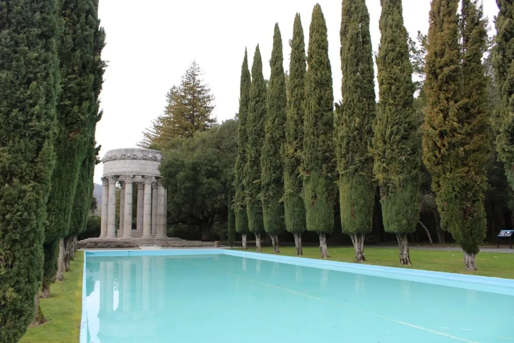 Reflective turquoise pool lined by cypress trees and classical temple in Bagni di Lucca