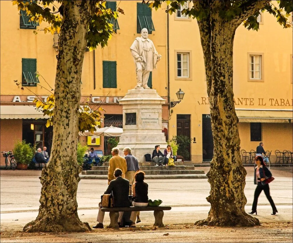 Couple sitting on bench under trees facing statue in Lucca piazza