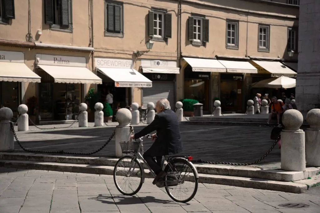 Elderly man cycling through Lucca piazza with stone bollards