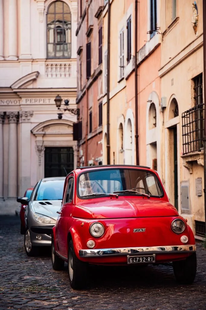 Classic red Fiat 500 parked along pastel buildings in Lucca
