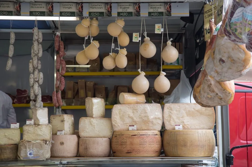 Market stall in Lucca stacked with aged cheeses and hanging cured meats.