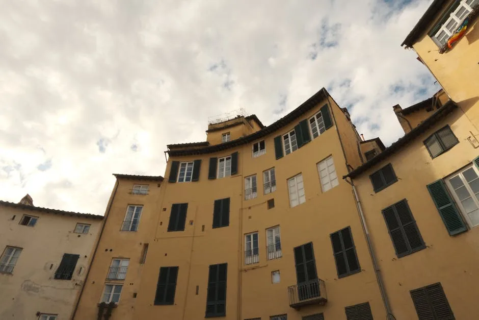 Curved yellow residential buildings rising under clouds in Lucca square