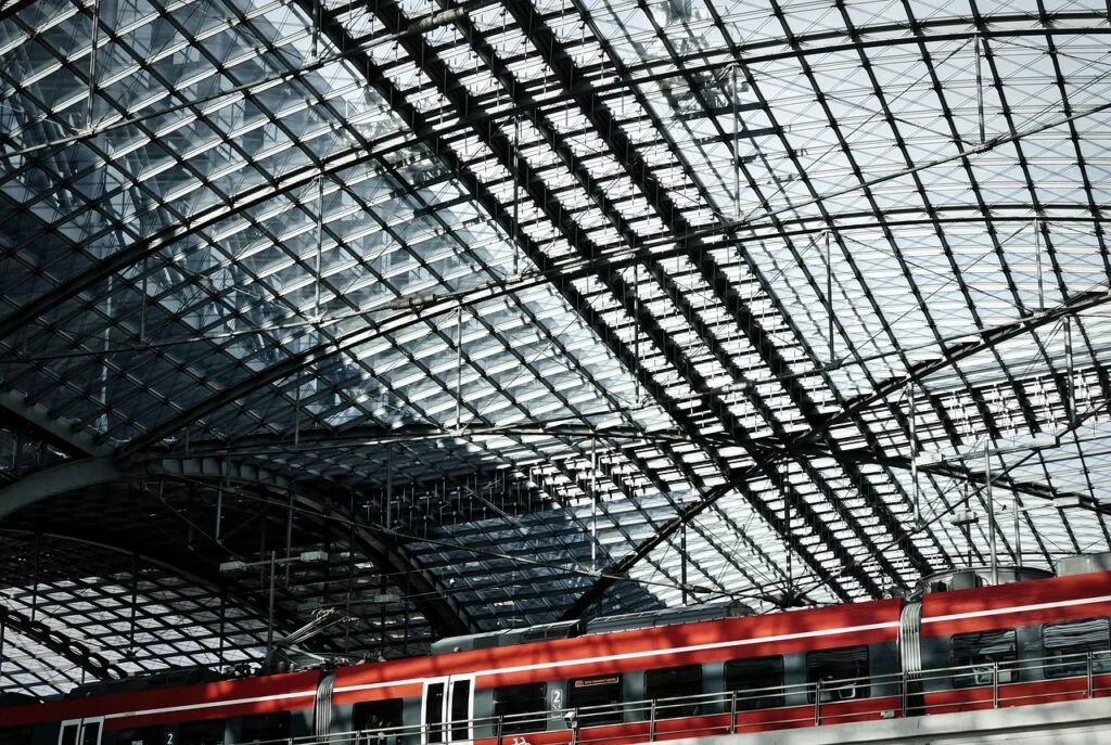 Red train beneath expansive glass roof of a modern station