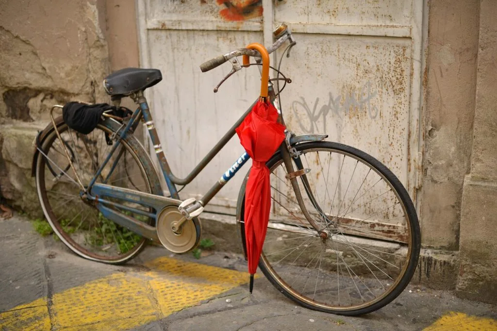 Old bicycle parked against wall in Lucca with red umbrella