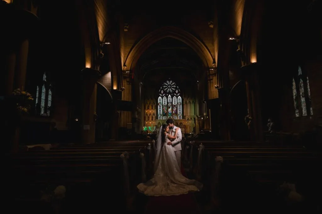Bride and groom embrace in dim Lucca church aisle under stained window