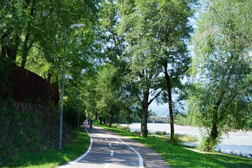 Tree-lined riverside bike path near Lucca with distant bridge
