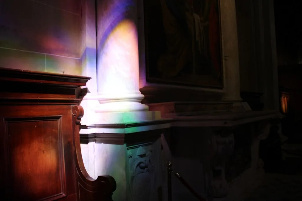 Rainbow-colored stained-glass light falling on a column in Lucca church