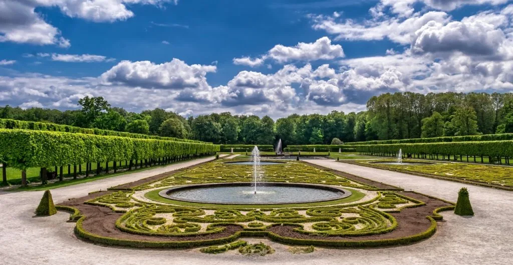 Ornamental parterre garden with circular fountain and manicured hedges under clouds