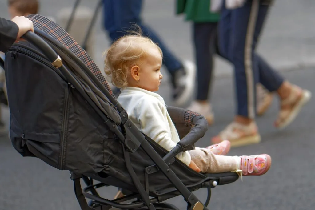 Blond toddler sitting in a stroller on a busy Lucca street