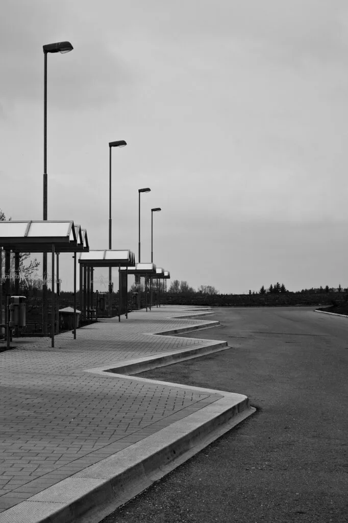 Row of empty bus shelters and tall lampposts under cloudy sky