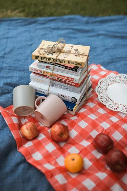 Stack of tied books, mugs and apples on checkered picnic blanket