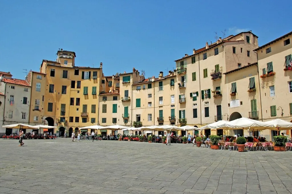 Piazza dell'Anfiteatro with curved yellow buildings and outdoor cafes in Lucca